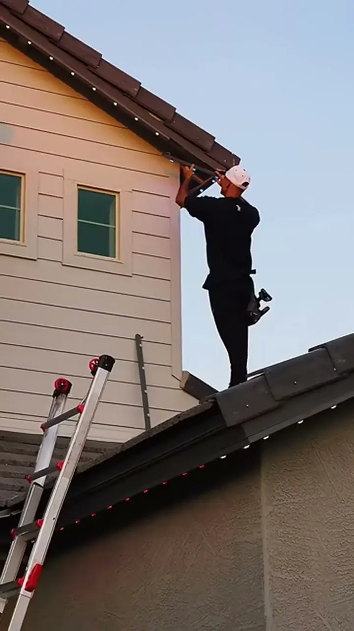 Installer on a ladder working along a roofline in daylight