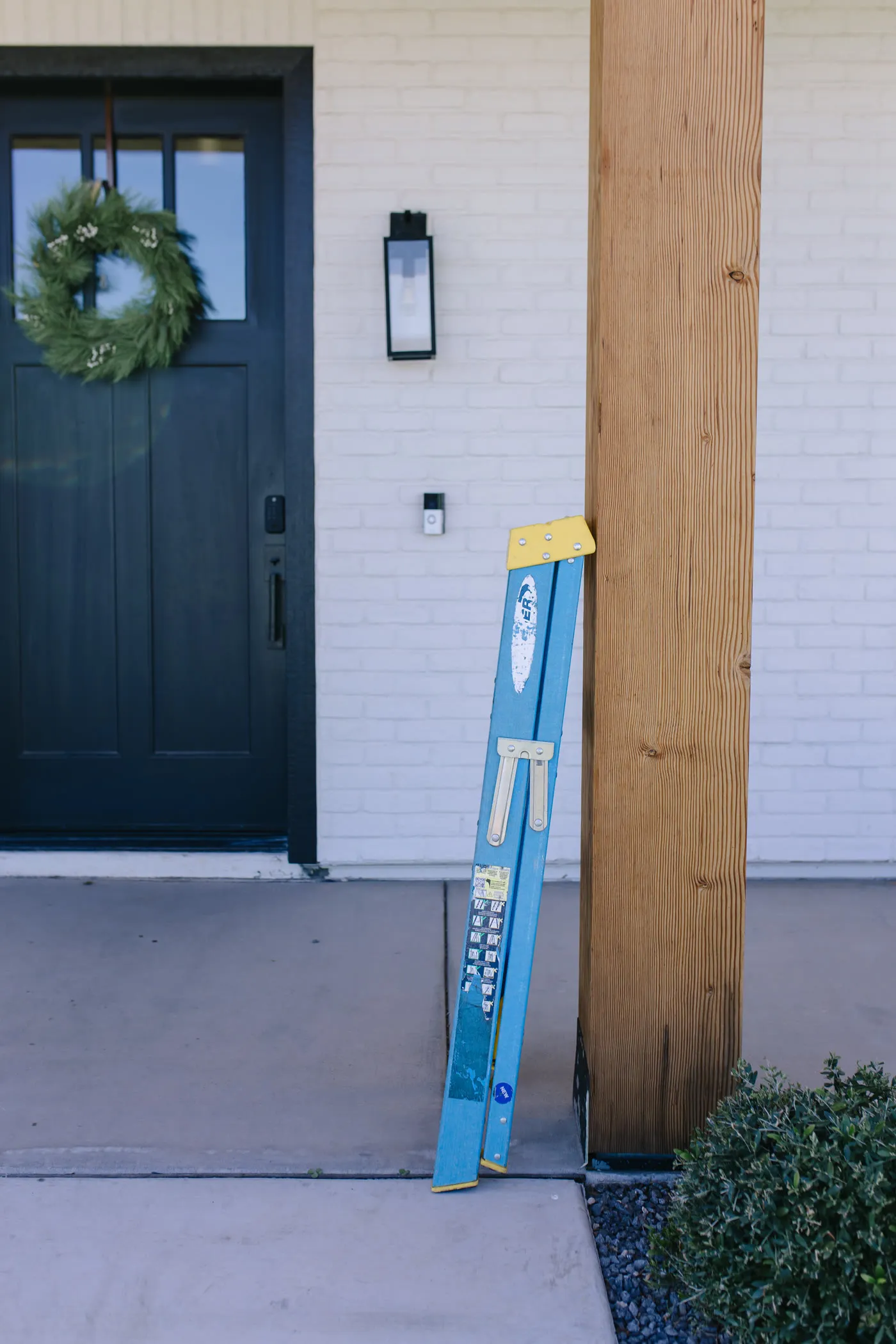 Ladder set up beside a front door hung with a holiday wreath