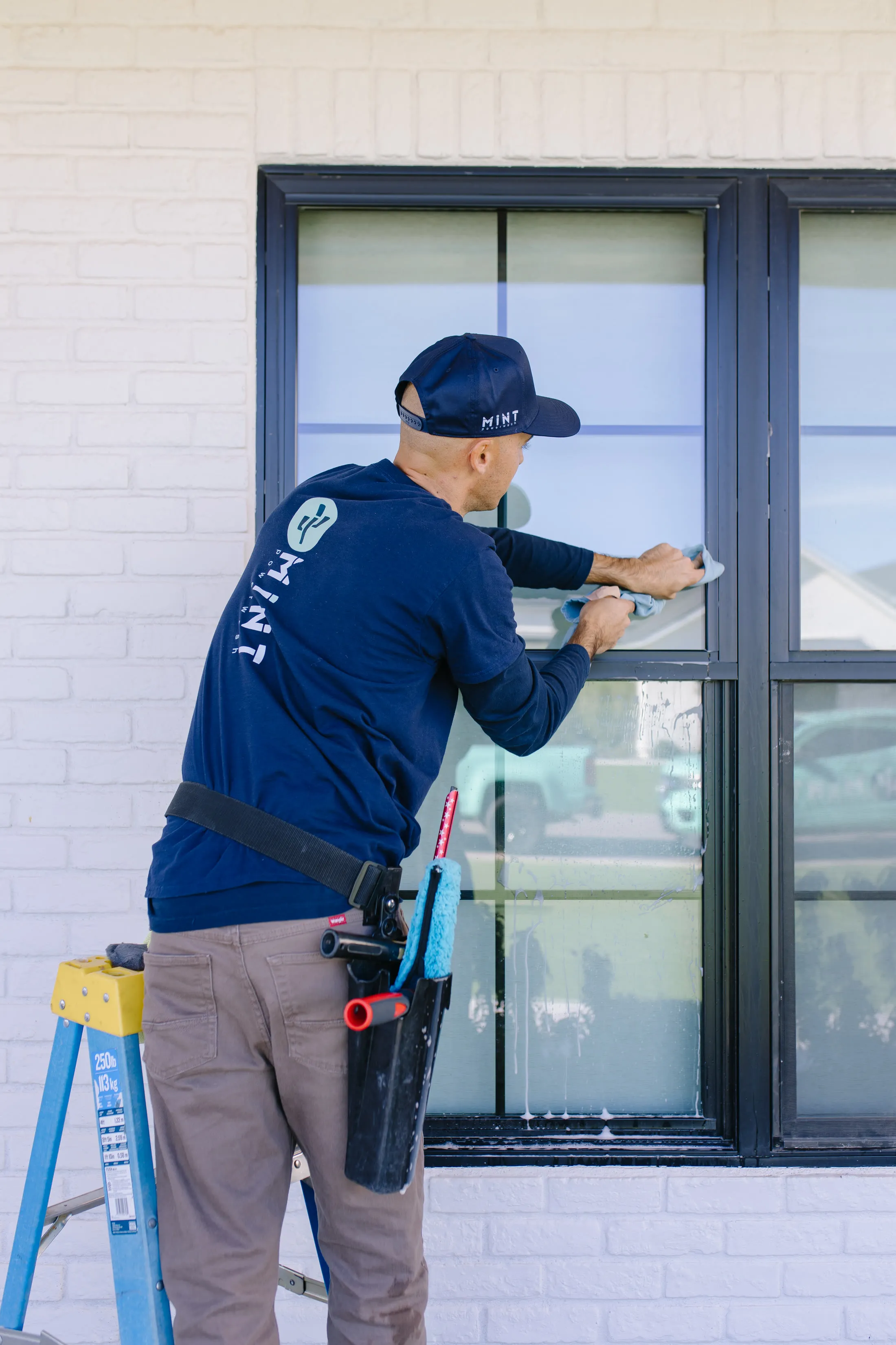 MiNT technician hand-detailing a window frame, tools on his belt